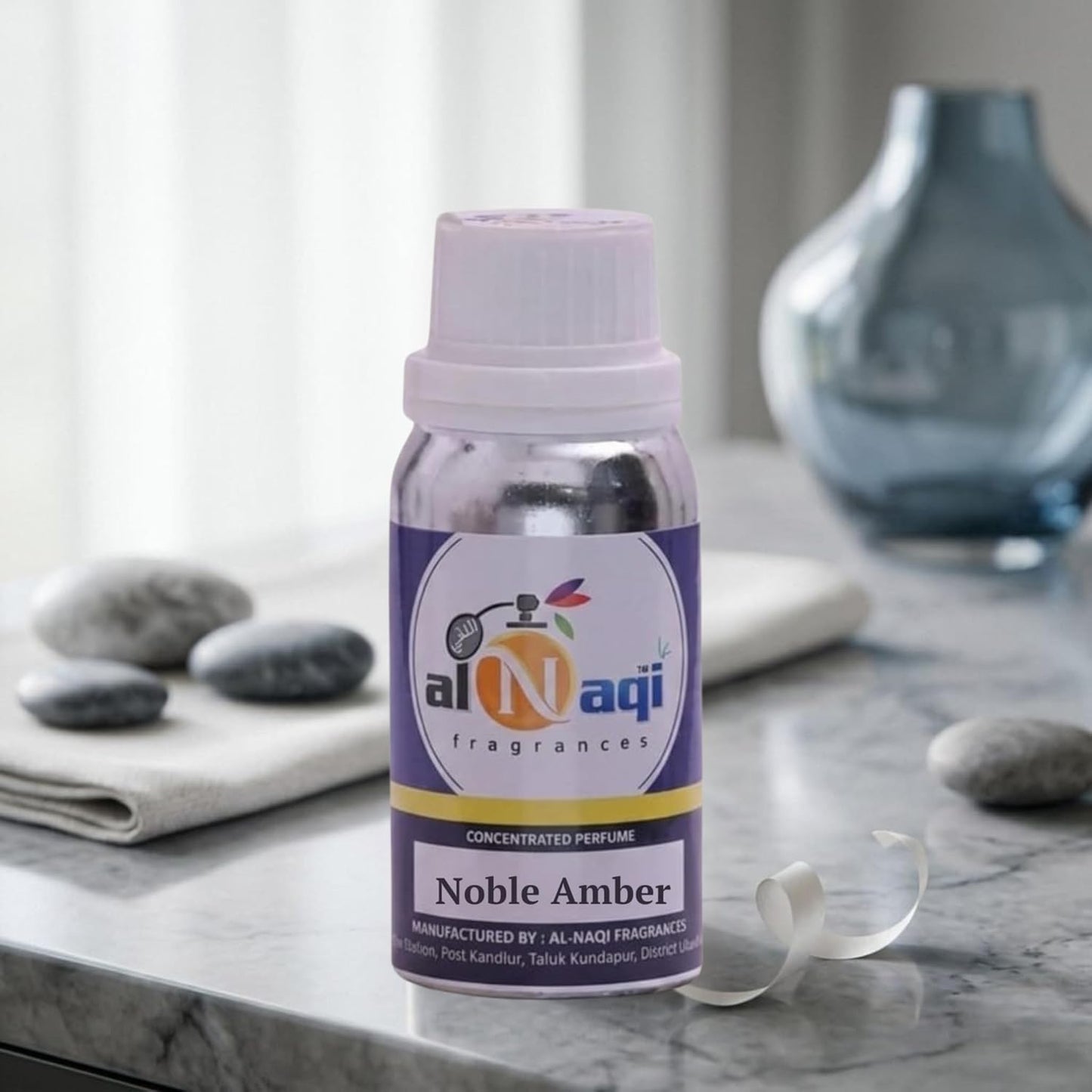 Bottle of Al-Naqi Noble Amber perfume on a marble surface with a vase and stones in the background.