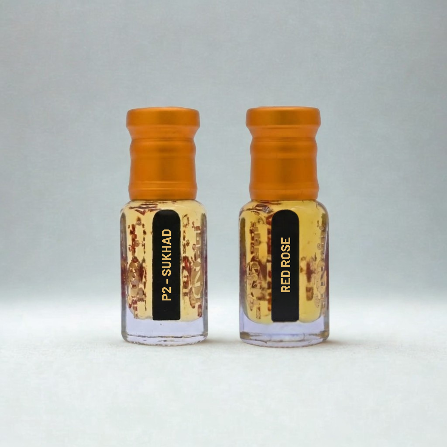 Two small glass bottles with orange caps labeled 'P2 Sukhadi' and 'Red Rose' on a light gray background.